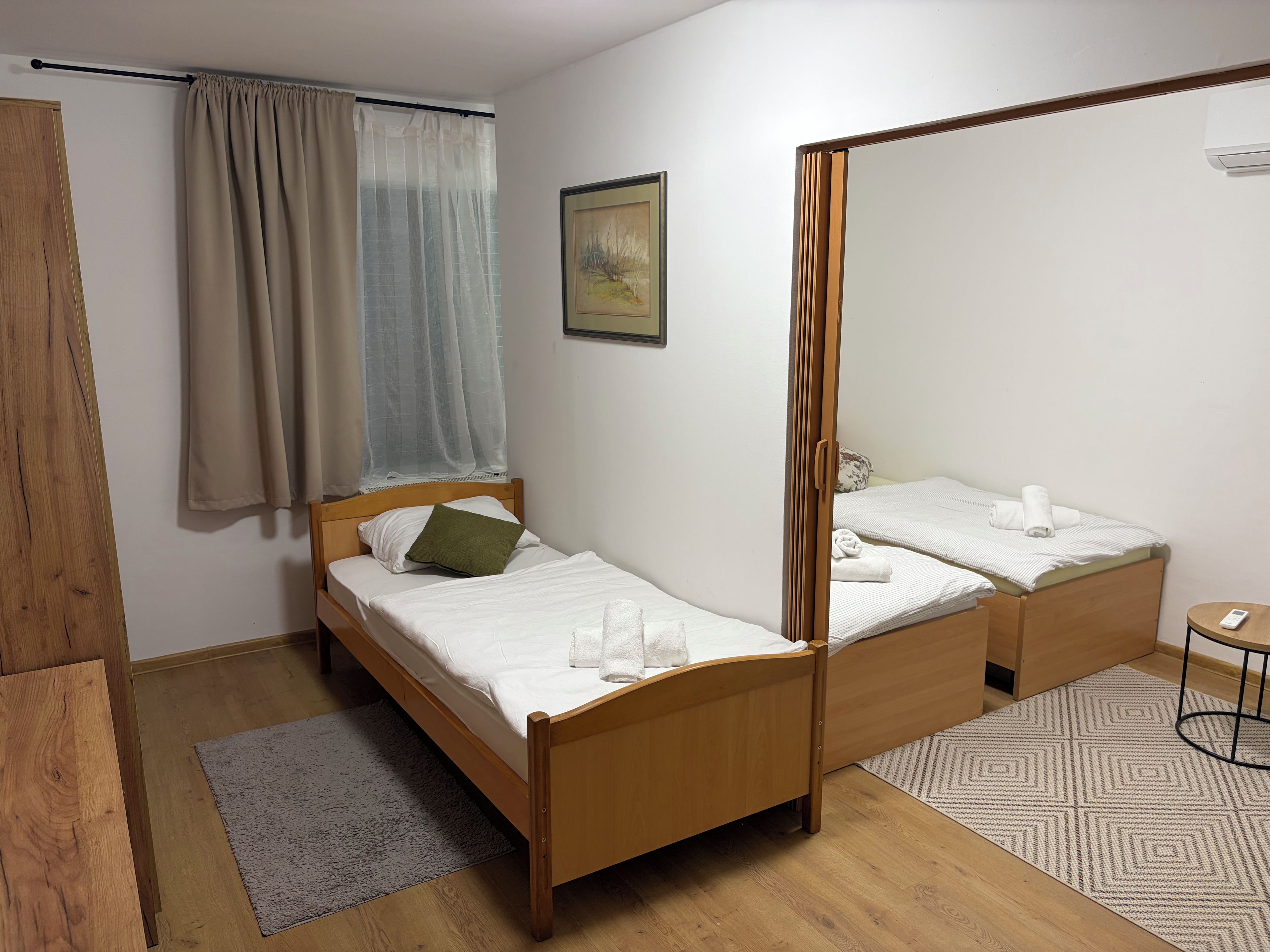 Una habitación con una cama de madera, un espejo, una mesita redonda y una ventana con cortinas.