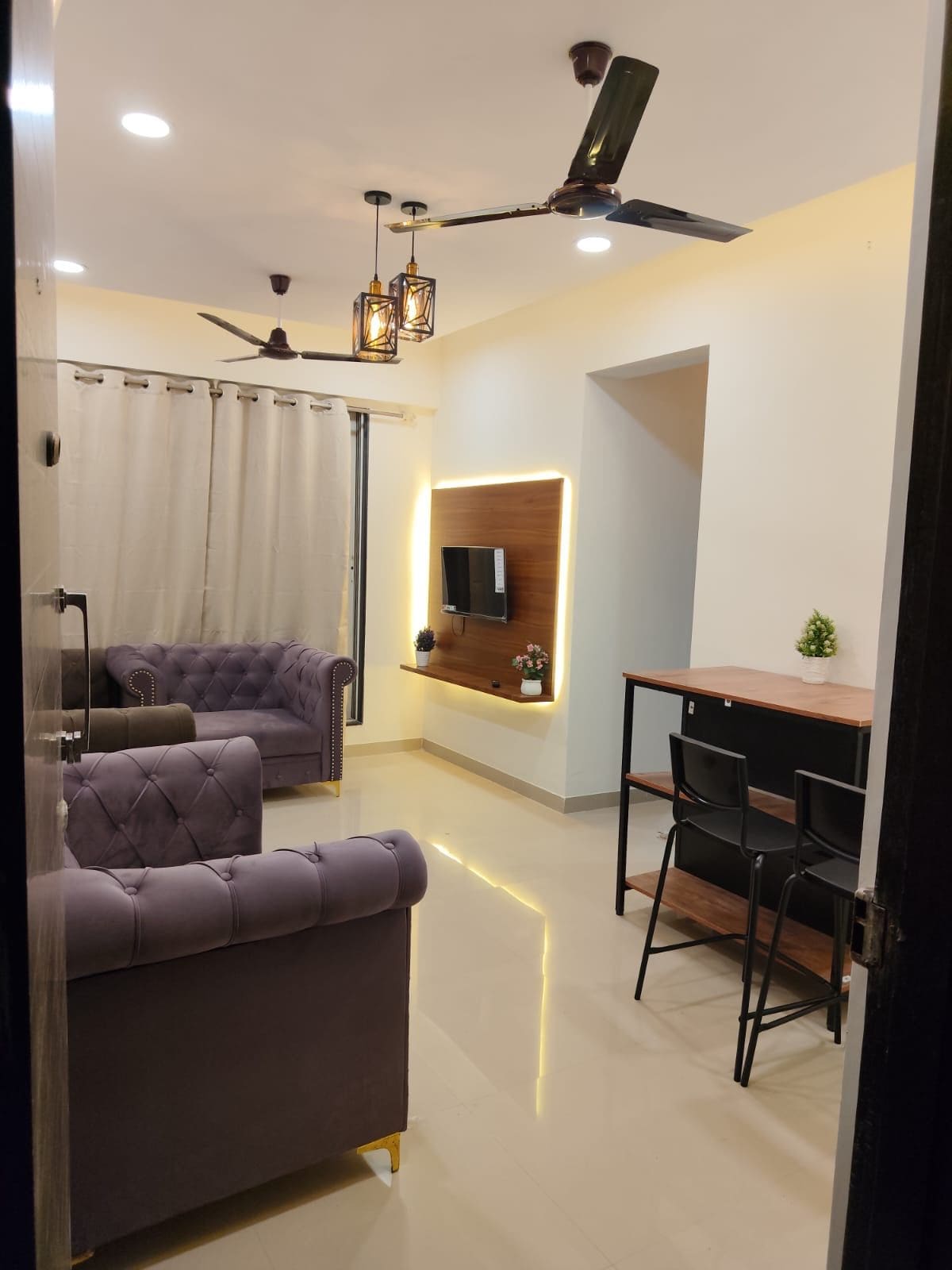 Uma sala de estar moderna com um sofá, uma mesa de jantar com cadeiras, um ventilador de teto e uma televisão na parede.