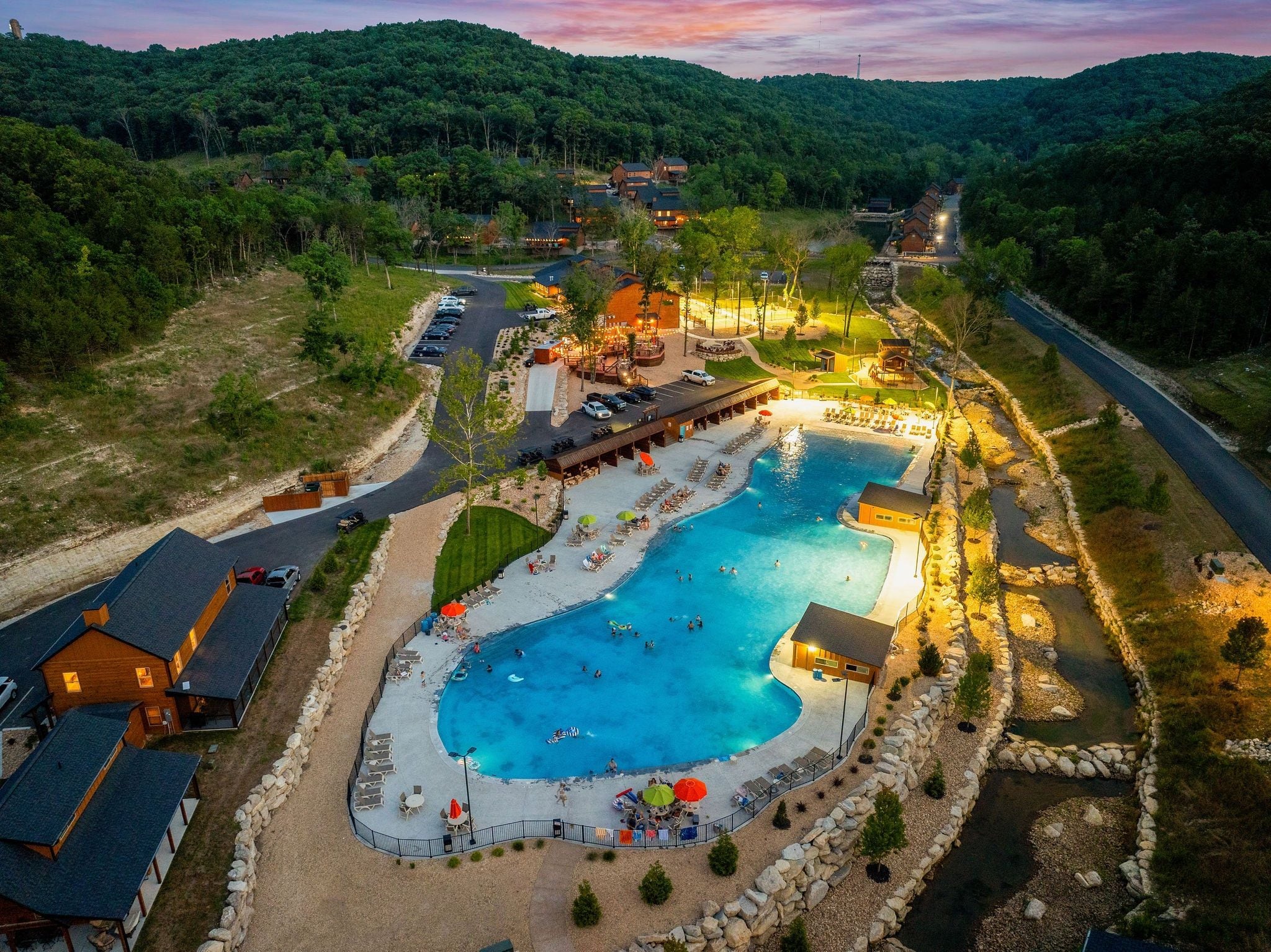 Un resort con una amplia piscina, varias habitaciones y vistas al bosque circundante.