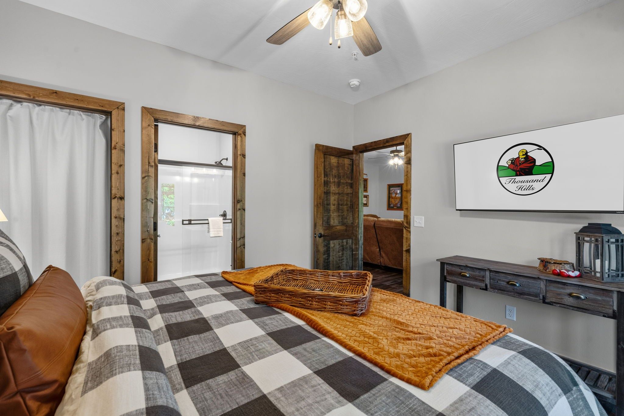 A bedroom with a bed, a wooden door, a mirror, a desk, and a television.