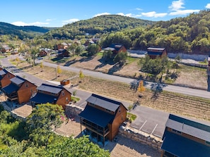 A residential area with multiple houses, a paved road, and a hilly landscape in the background. - 3-Level Luxury Cabin 🌲 Creek Views, Hot Tub & Top-Tier Resort Pools! (Hollister)