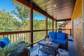 A covered outdoor seating area with a view of a forested landscape. - 3-Level Luxury Cabin 🌲 Creek Views, Hot Tub & Top-Tier Resort Pools! (Hollister)