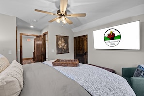 A bedroom with a bed, a ceiling fan, a wall-mounted TV, and a door with a wooden frame. - 3-Level Luxury Cabin 🌲 Creek Views, Hot Tub & Top-Tier Resort Pools! (Hollister)