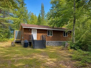 A cabin with a wooden exterior, a front door, and a small porch. - Turtle Cabin – Gichigami Island Properties 2 Bedrooms • 1 Bathroom • Sleeps 4 • Beach Access (La Pointe)