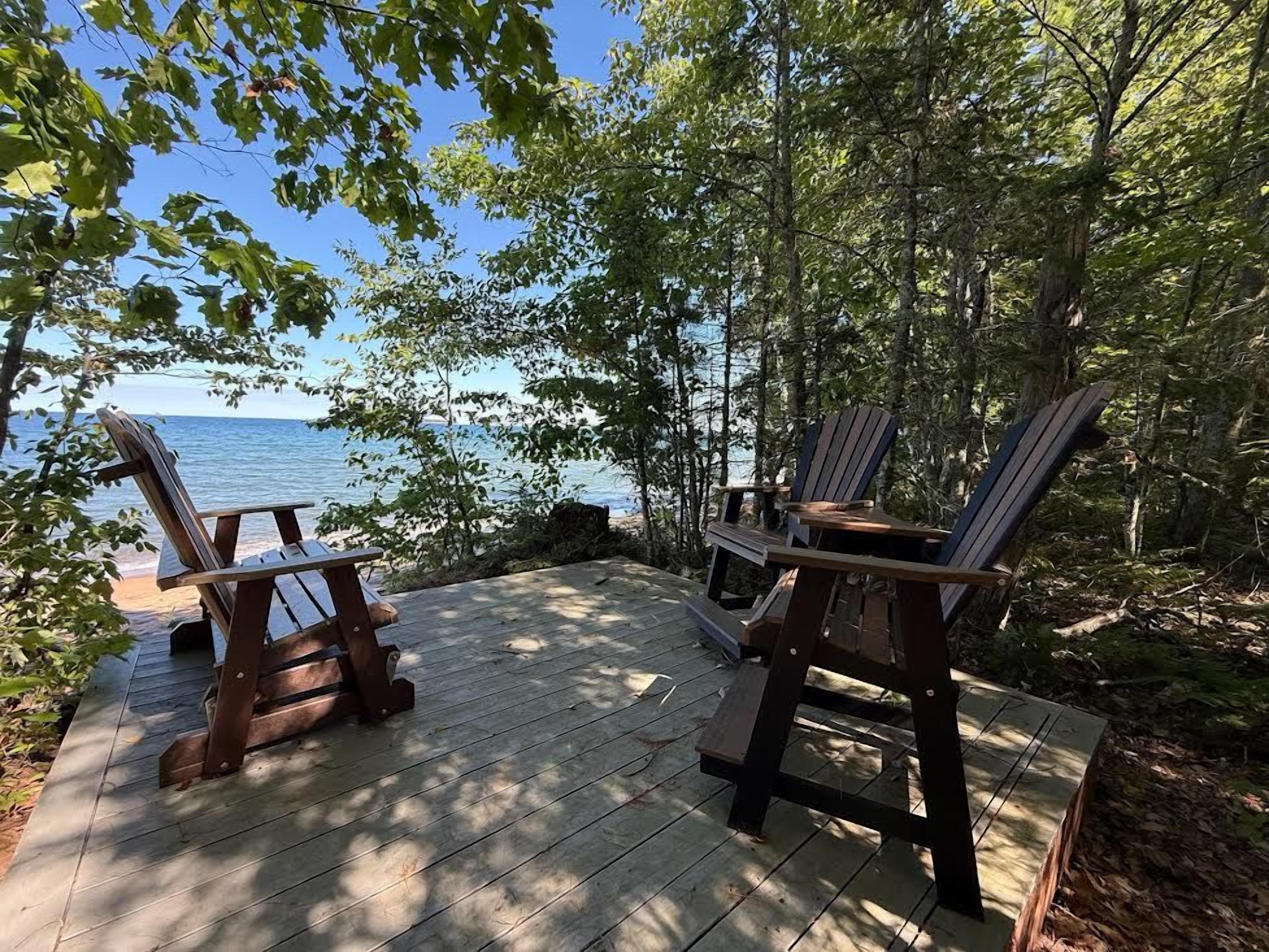 A wooden deck with Adirondack chairs overlooking a body of water.
