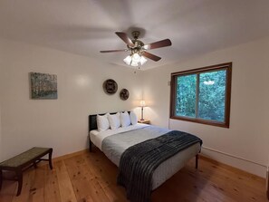 Ein Schlafzimmer mit einem Bett, einem Deckenventilator, einem Nachttisch, einer Lampe, einem Fenster und einem Bild an der Wand.