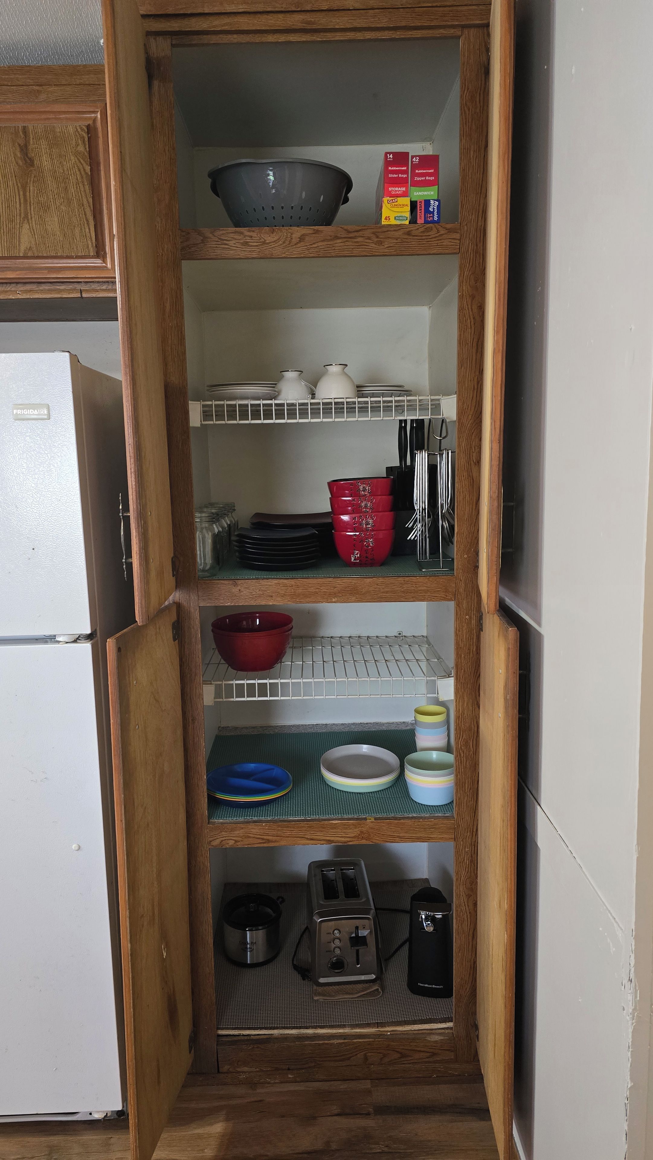 Un garde-manger de cuisine avec des étagères contenant des boîtes de rangement, des bols, des assiettes et un grille-pain.