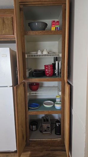 A kitchen pantry with shelves containing storage containers, bowls, plates, and a toaster.