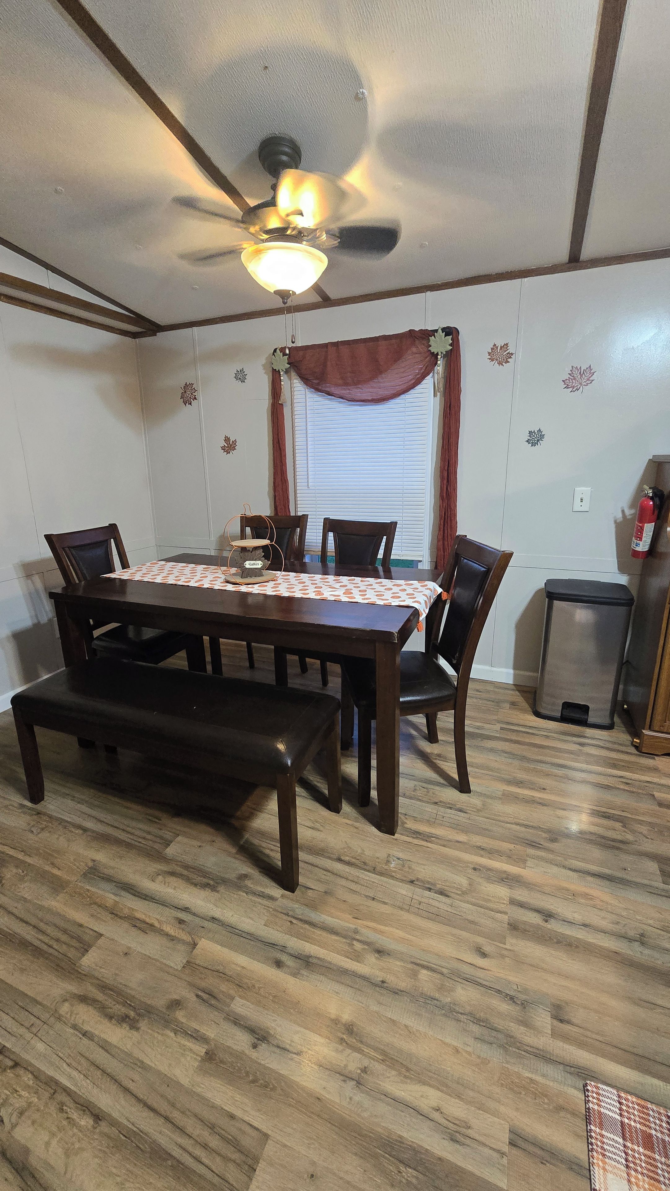 A dining area with a wooden table, chairs, a ceiling fan, and a window with curtains.