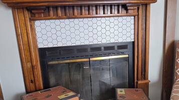 Uma lareira com manto de madeira, parte superior em azulejos e duas malas colocadas na frente.