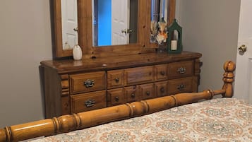 A bedroom with a wooden dresser, a large mirror, and a patterned bedspread.