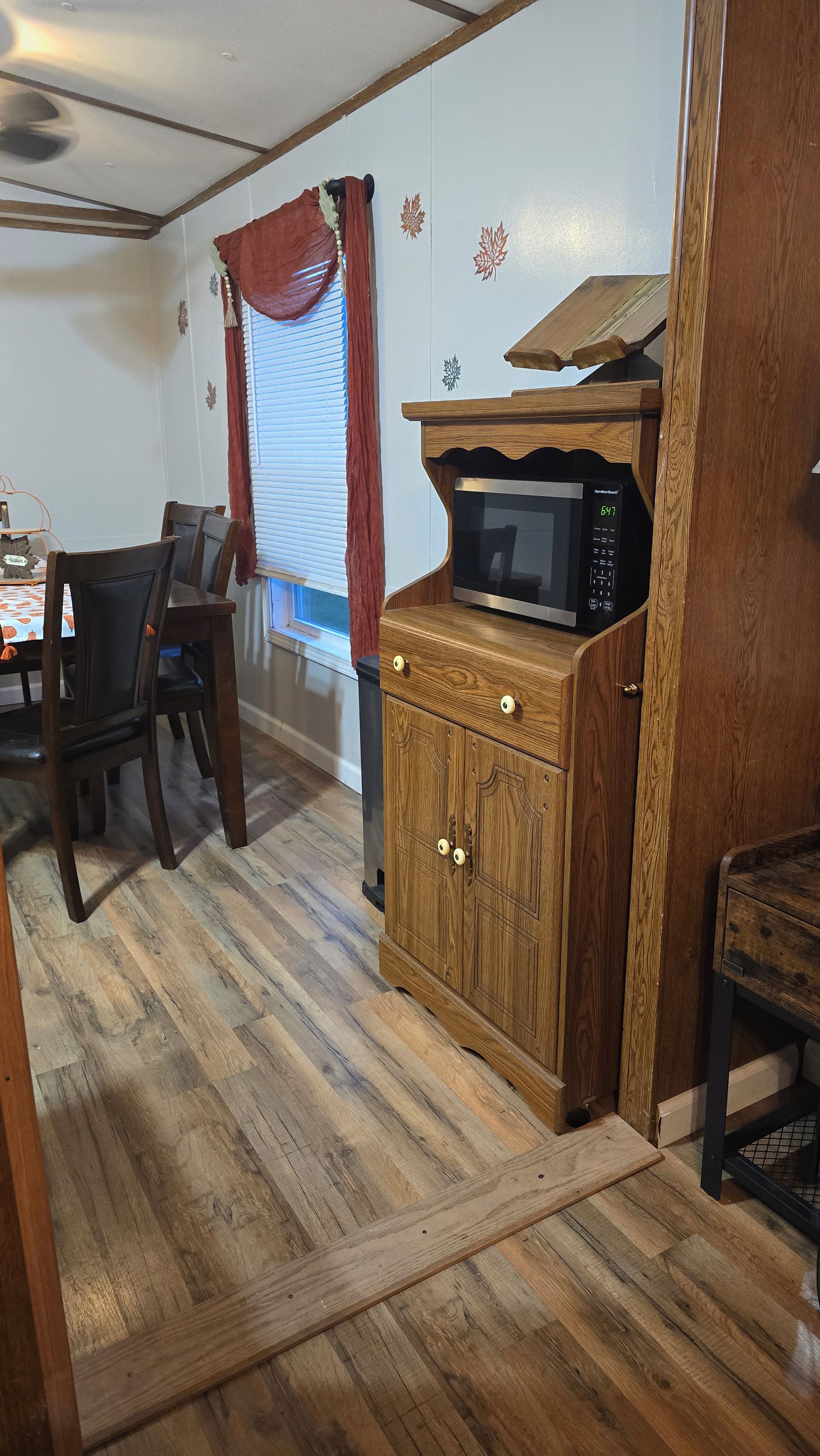 Un comedor con un armario de madera, un microondas y una mesa con sillas.