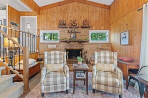 A cozy living room with a fireplace, two plaid armchairs, a small table, and a staircase. - Legacy Landing at Lake Guntersville (Guntersville)