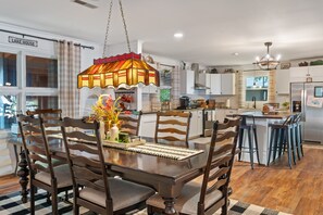 A modern kitchen with white cabinets, a dining table with chairs, and a hanging light fixture.