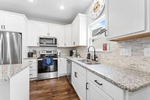 Una cocina moderna con armarios blancos, electrodomésticos de acero inoxidable, encimeras de granito y suelo de madera.