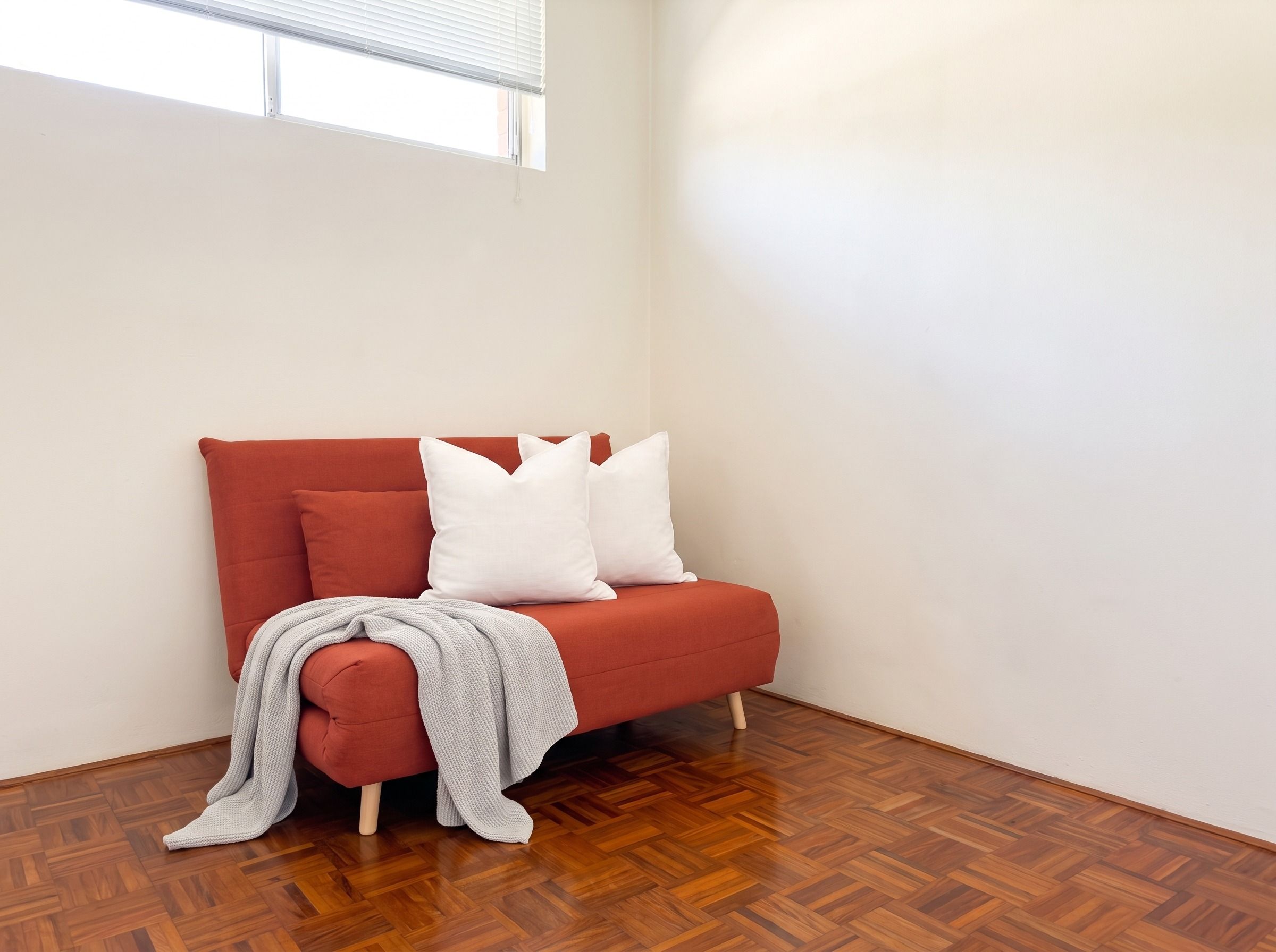 Une pièce d’angle avec un canapé rouge, des coussins blancs et un plaid gris.