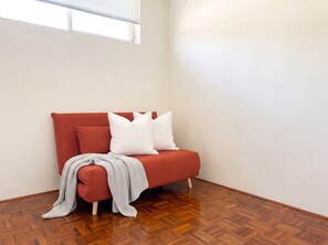 Une pièce d’angle avec un canapé rouge, des coussins blancs et un plaid gris.