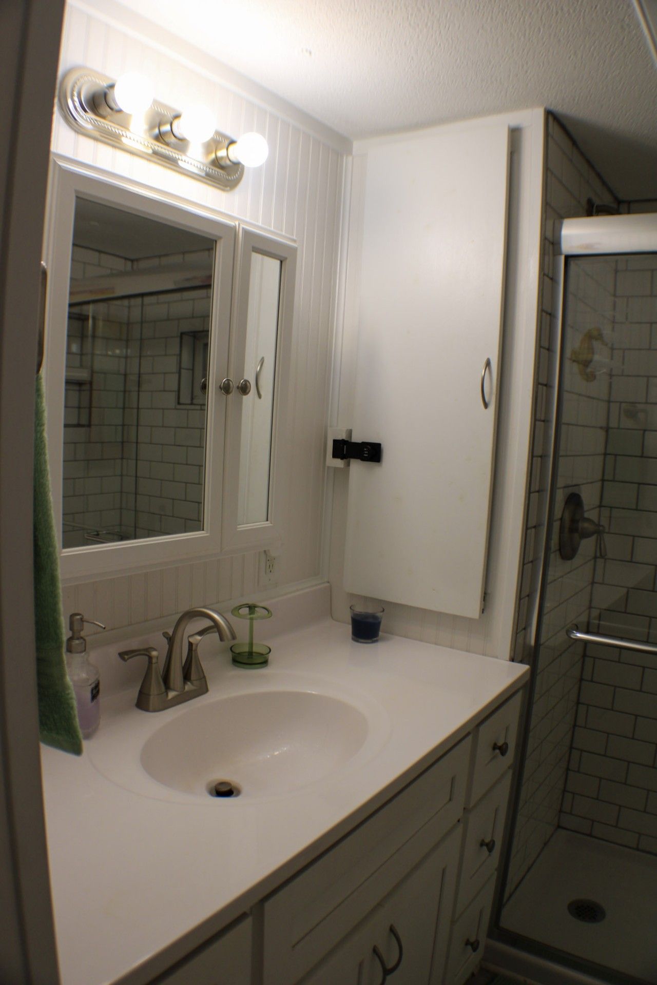 Een badkamer met een wastafel, spiegel, kast en douche.