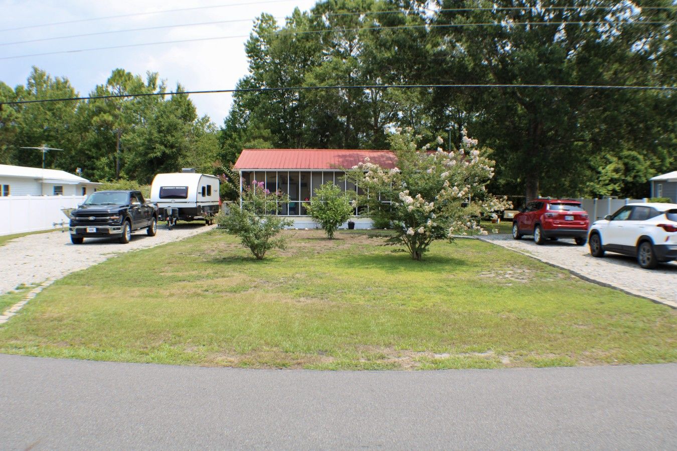 A residential area with a red-roofed building, a grassy lawn, and parked vehicles including a truck and cars.