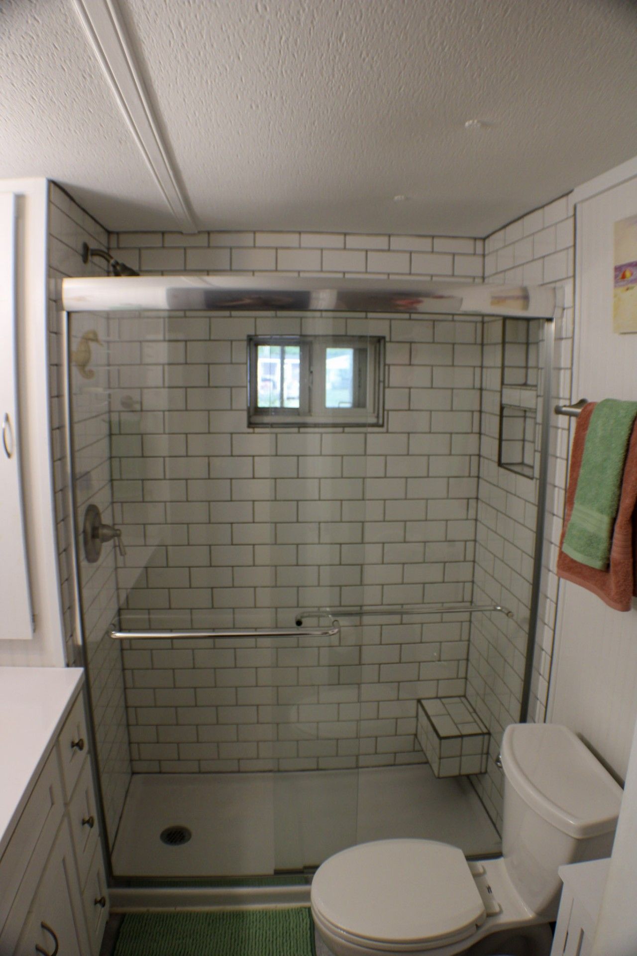 A small, enclosed shower area with a glass door, a toilet, and a small window above the shower.