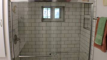 A small, enclosed shower area with a glass door, a toilet, and a small window above the shower.