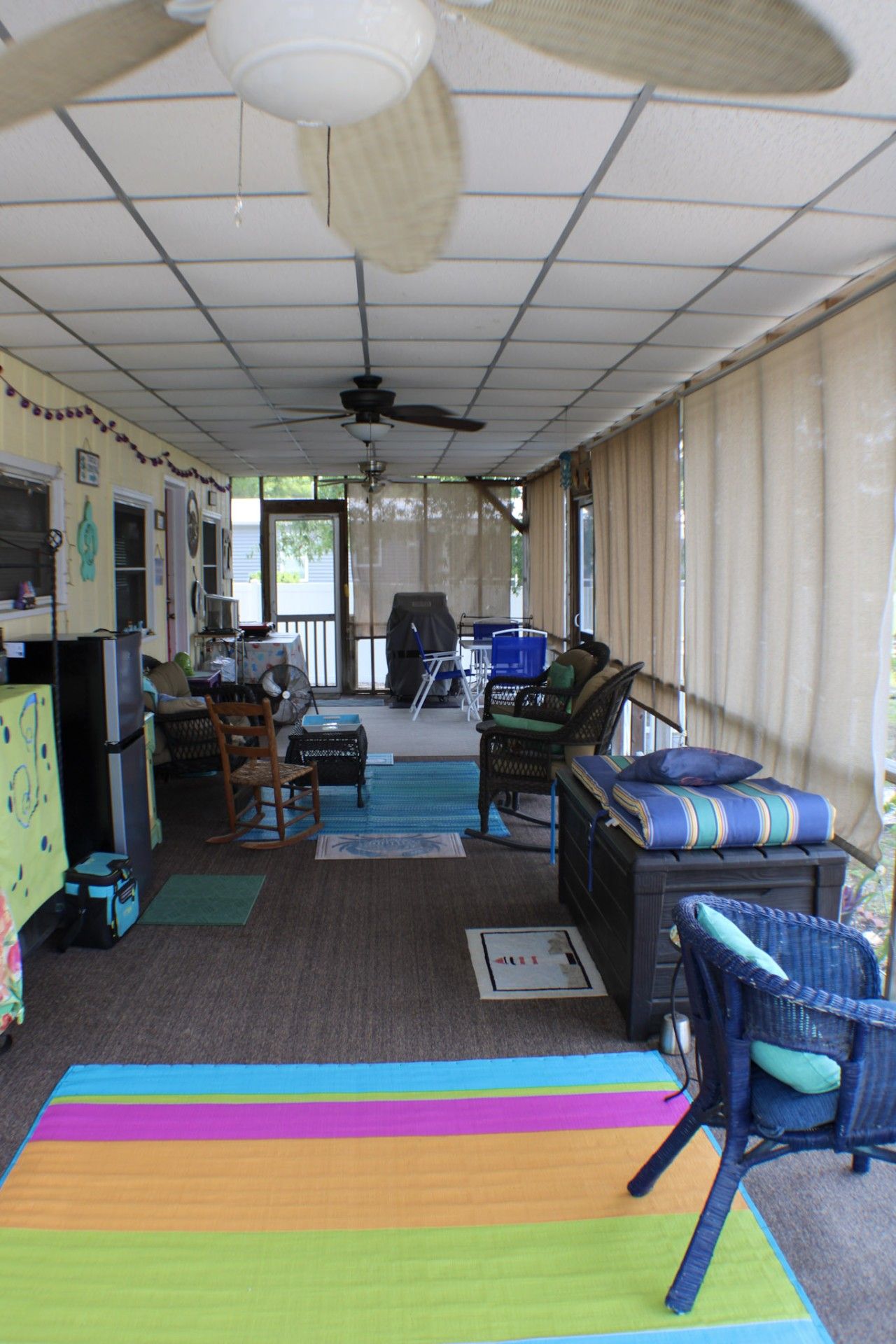 Un espace extérieur abrité, doté d’un ventilateur de plafond, d’une table à manger, de chaises et d’un tapis coloré.