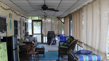 Un espace extérieur abrité, doté d’un ventilateur de plafond, d’une table à manger, de chaises et d’un tapis coloré.