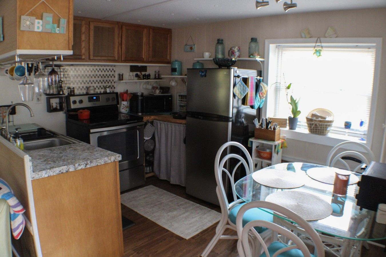 A compact kitchen with wooden cabinets, a stainless steel refrigerator, and a dining area with a glass table and chairs.