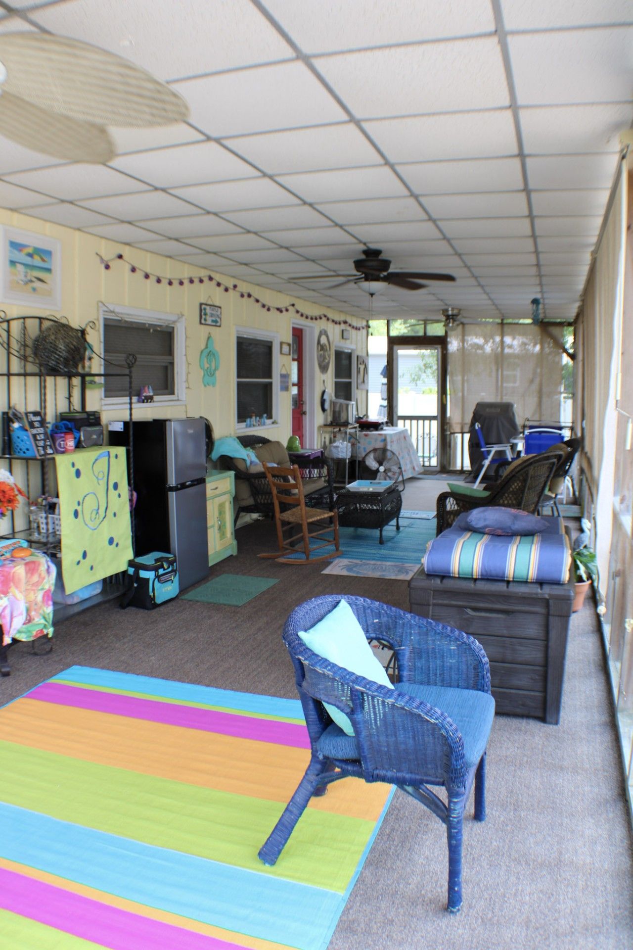 A covered outdoor living space with a ceiling fan, a refrigerator, a dining table, and various seating arrangements including a rocking chair and a sofa.