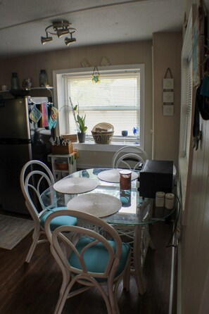 A compact kitchen with a dining table, chairs, a refrigerator, and a window with blinds.