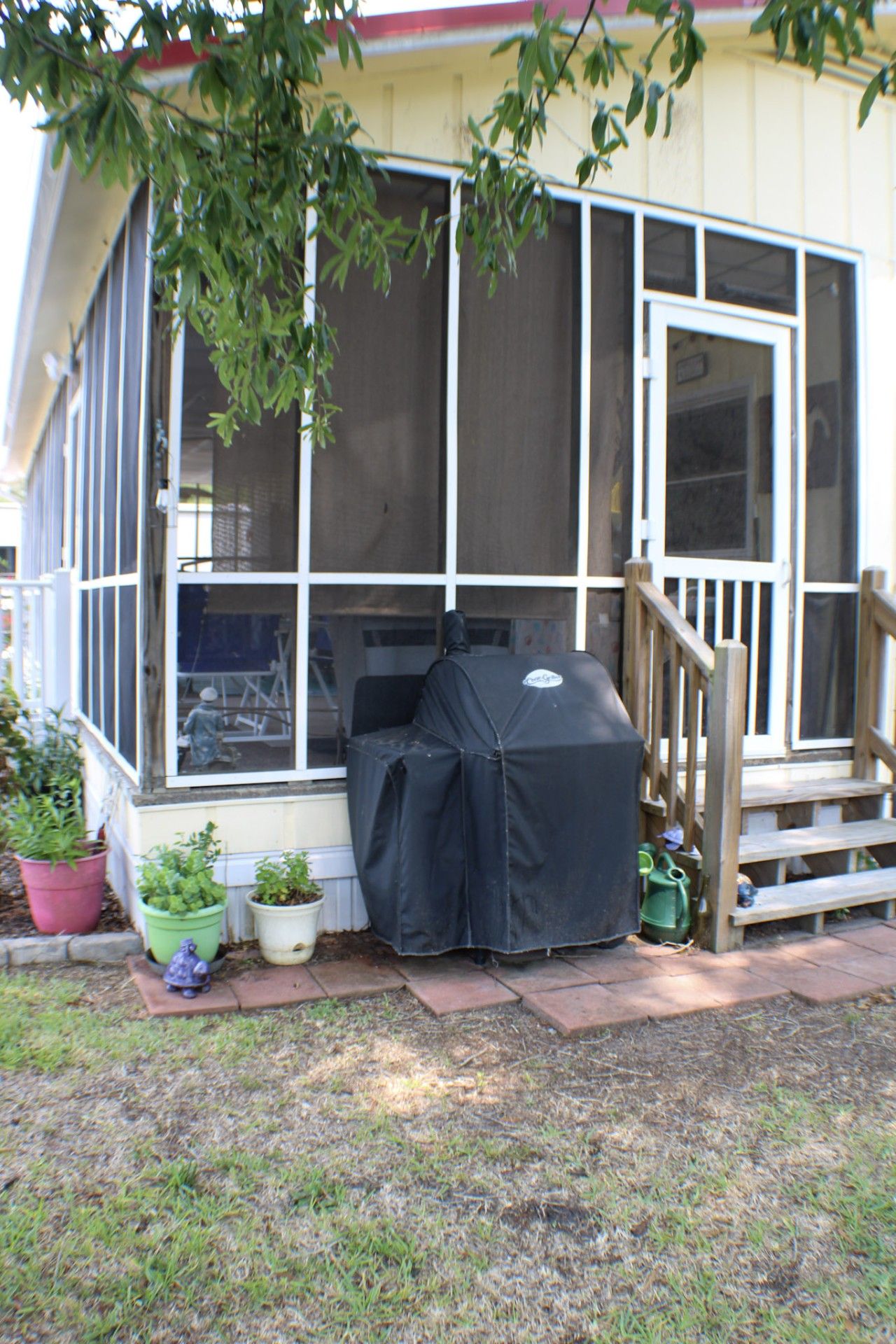 A covered porch with a grill, potted plants, and a wooden staircase.