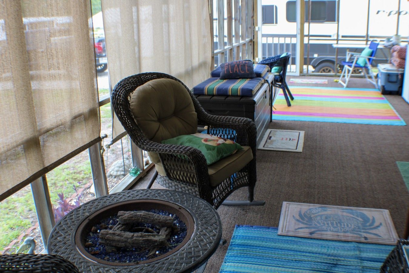 A covered outdoor seating area with wicker chairs, a fire pit, and colorful rugs.