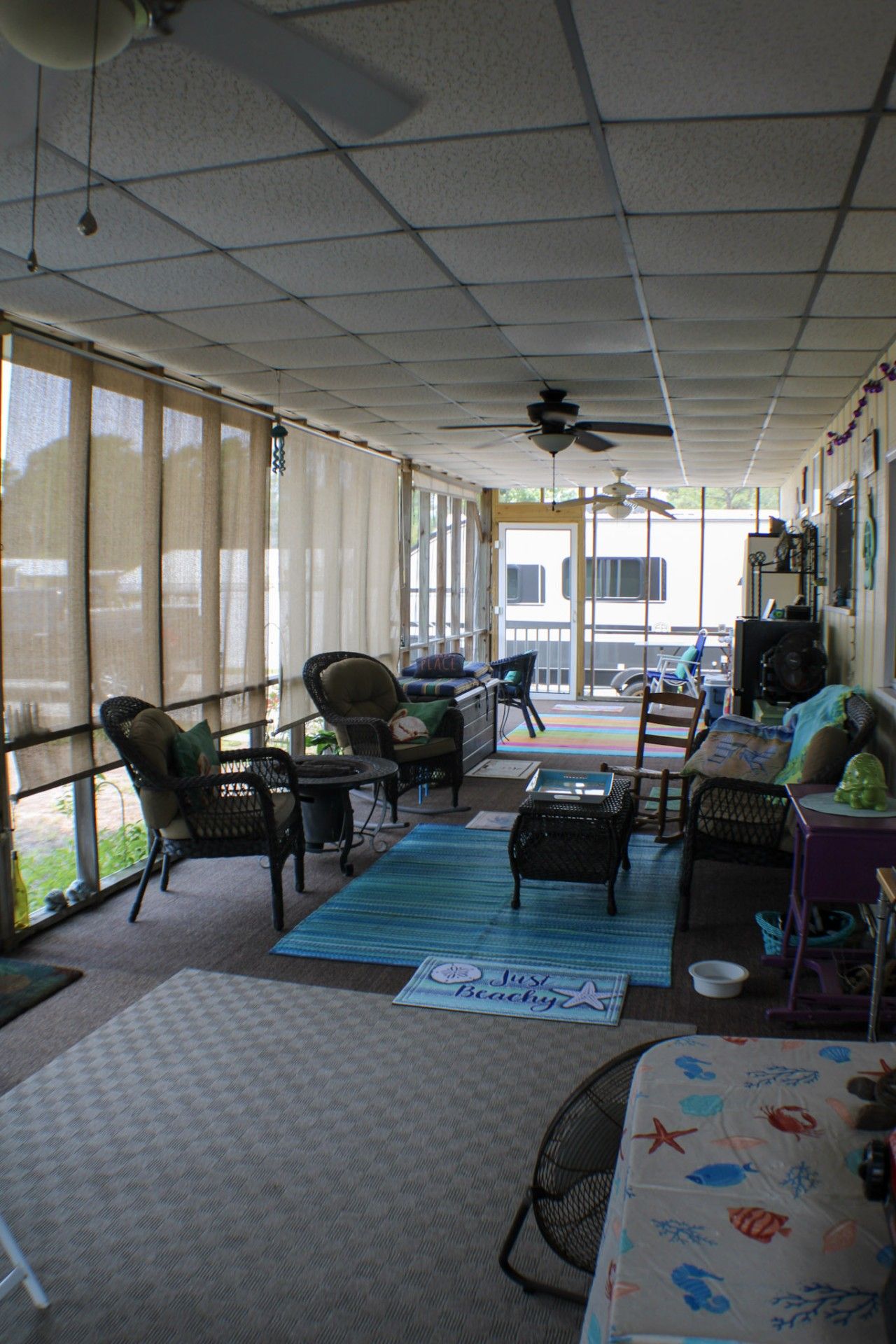A covered patio area with ceiling fans, wicker furniture, and a view of the outside.