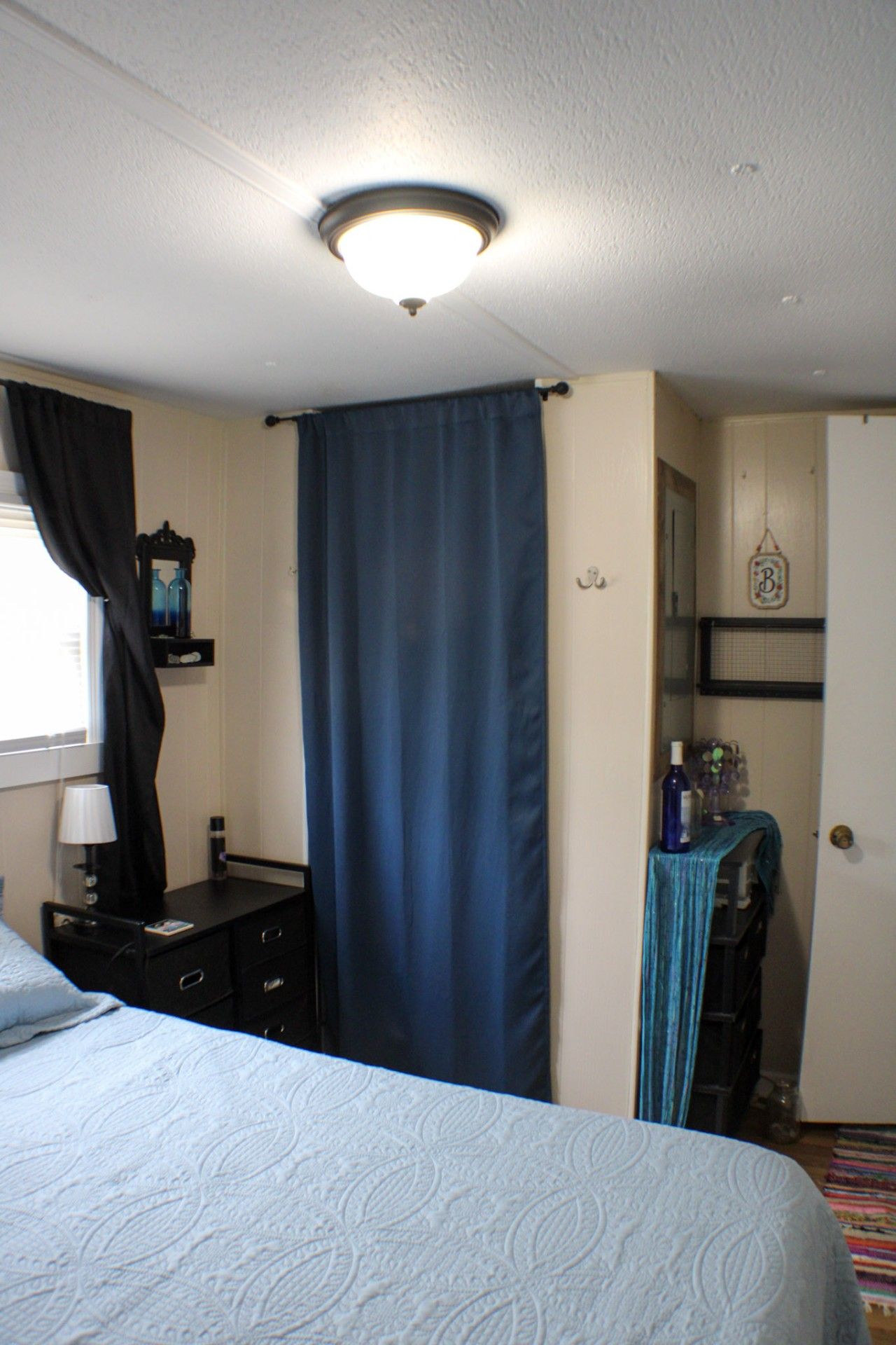 Una habitación de hotel con cama, escritorio, armario y ventana con cortinas.