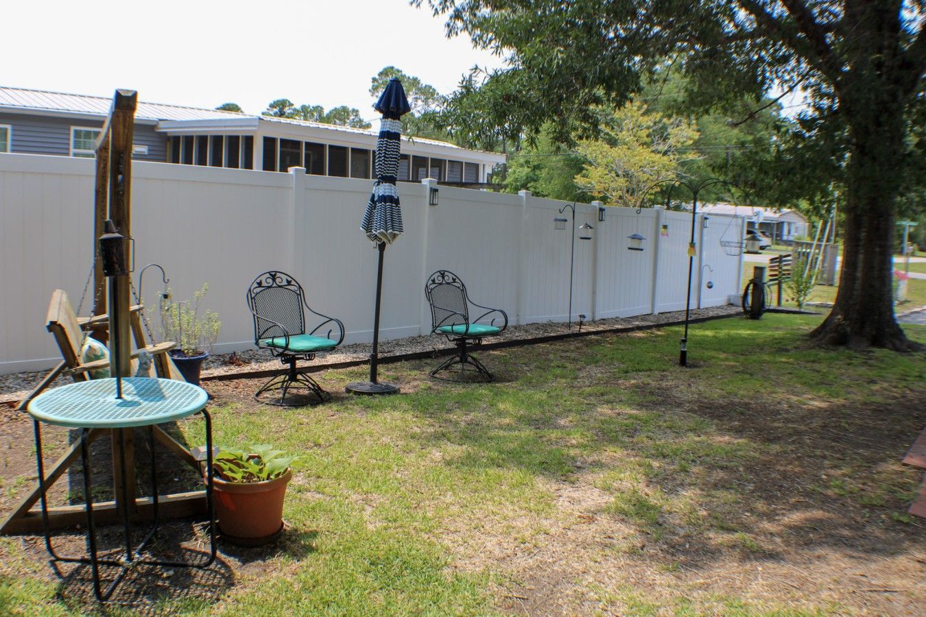 An outdoor seating area with metal chairs and a table, a white fence, and a tree.