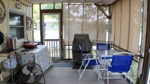 En overdækket terrasse med et bord, stole, grill og ventilator.