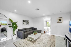 A modern living room with a grey sectional sofa, a white coffee table, and a large potted plant. - The Coastal Retreat. Spacious 5-bedroom House Near Ocean, Heated Pool And Studio (Pompano Beach)