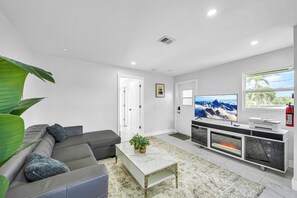 Ein modernes Wohnzimmer mit einem grauen Sofa, einem Couchtisch, einem Fernseher und einem Kamin.