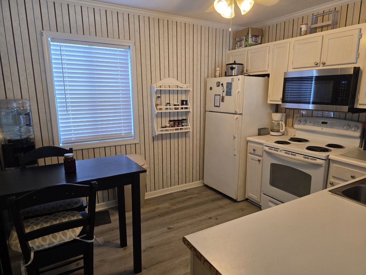 A kitchen with a stove, microwave, refrigerator, and a window with blinds.
