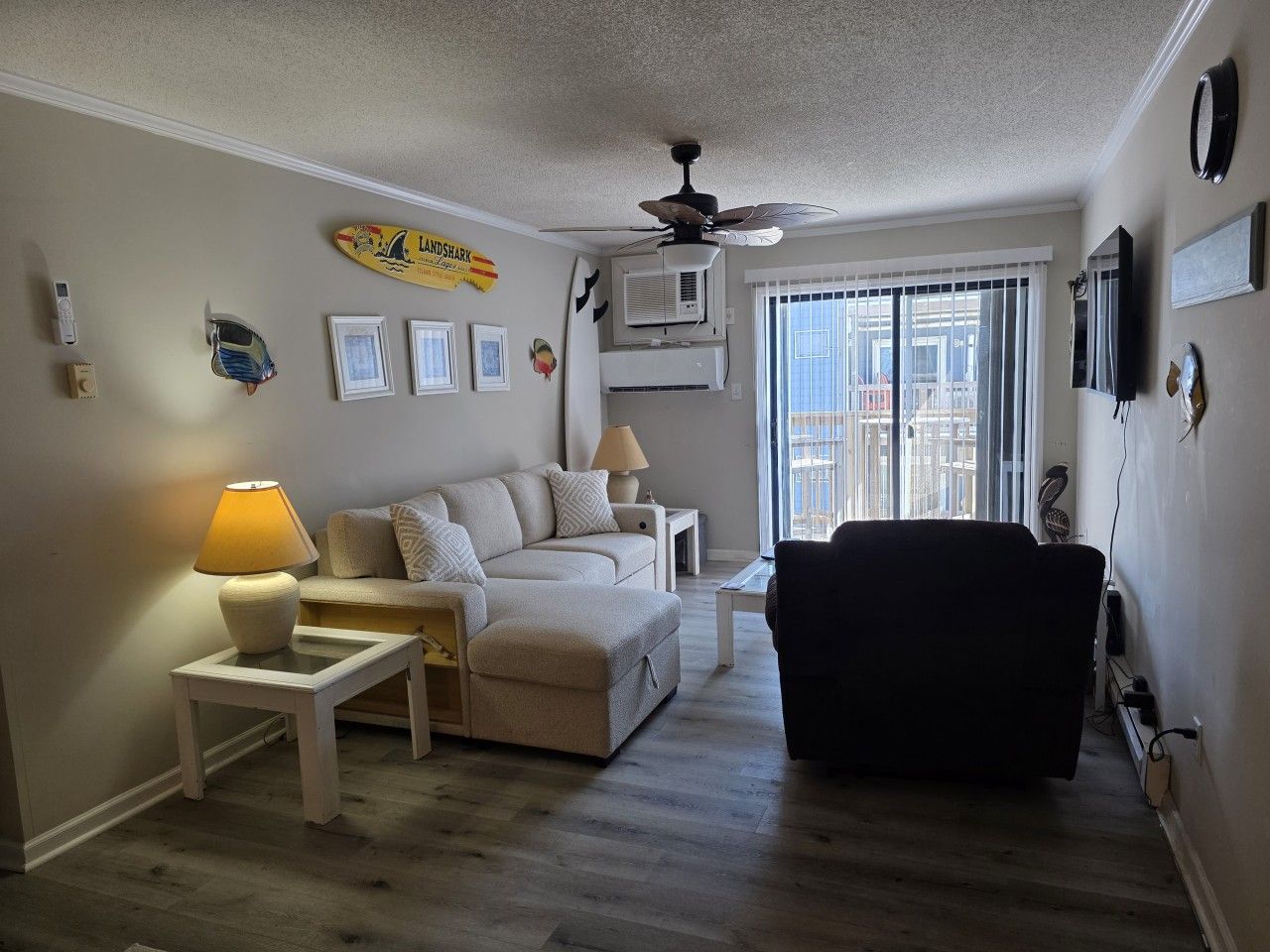 A living room with a sofa, ottoman, side tables, a ceiling fan, and a window with blinds.