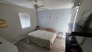 A bedroom with a bed, a ceiling fan, a window with blinds, and a wall with framed pictures. - Beach Retreat Oceanview Balcony (North Topsail Beach)