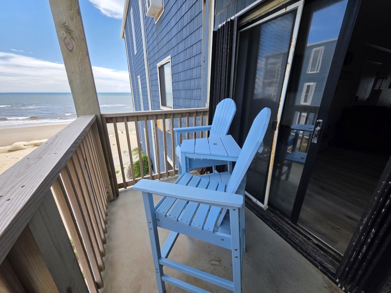 A wooden deck with two Adirondack chairs, a glass door, and a view of the beach.