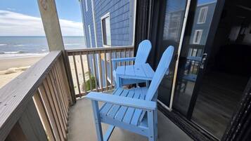 A wooden deck with two Adirondack chairs, a glass door, and a view of the beach.