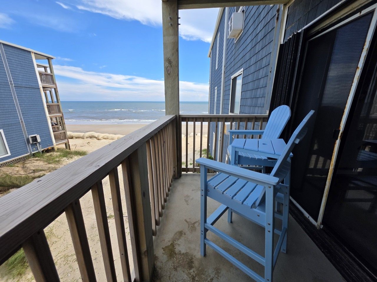 Een balkon met uitzicht op het strand, een blauwe stoel en een gebouw met een luik.