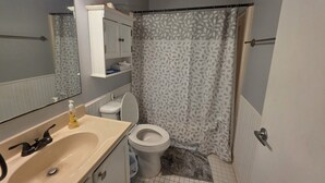 A bathroom with a toilet, sink, mirror, and shower curtain. - Beach Retreat Oceanview Balcony (North Topsail Beach)