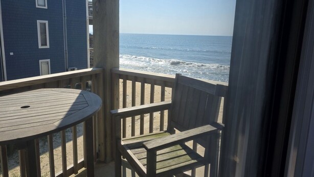 A balcony with a view of the ocean, a round wooden table, and two wooden chairs. - Beach Retreat Oceanview Balcony (North Topsail Beach)