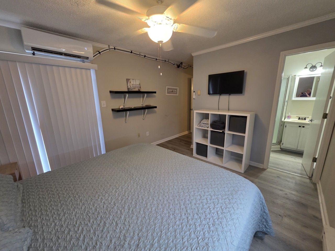 A bedroom with a bed, a TV, a built-in shelf unit, and a bathroom visible through an open door.