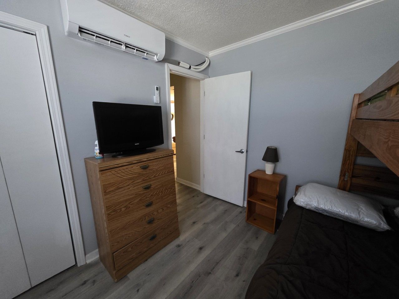 A bedroom with a wooden dresser, a television on top, a bedside table with a lamp, and a bunk bed.