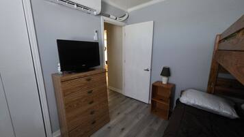A bedroom with a wooden dresser, a television on top, a bedside table with a lamp, and a bunk bed.