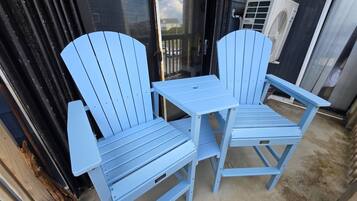 Zwei blaue Adirondack-Stühle und ein kleiner Tisch vor einem Gebäude mit einer schwarzen Tür und einer Klimaanlage.